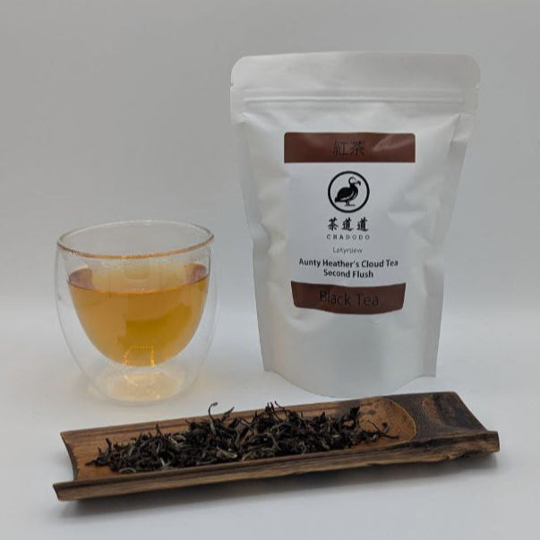 Aunty Heather's Cloud Tea Second Flush packaging with a glass of tea and a bamboo tea scoop with loose-leaf tea on it